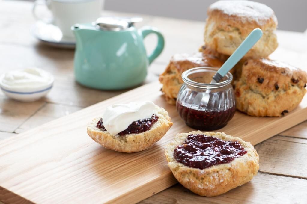 A wooden board with scones and jam, a teapot, and a cup on a table.
