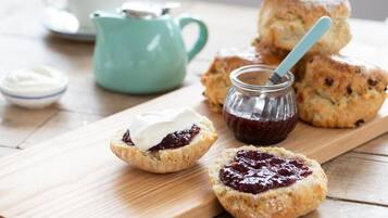 A wooden board with scones and jam, a teapot, and a cup on a table.