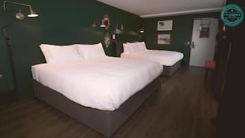 A hotel room with two beds, dark wooden flooring, green walls, and wall-mounted lighting.