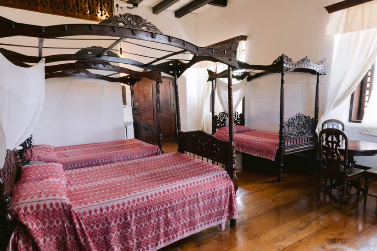 Una cama tradicional con dosel, suelo de madera y una clásica silla de madera.