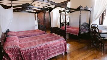 Een traditioneel hemelbed met baldakijn, een houten vloer en een klassieke houten stoel.