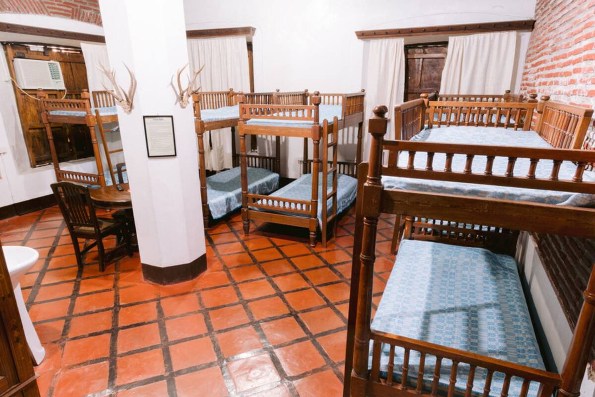 Una habitación con cuatro literas de madera, una mesa de madera con sillas y suelo de baldosas.