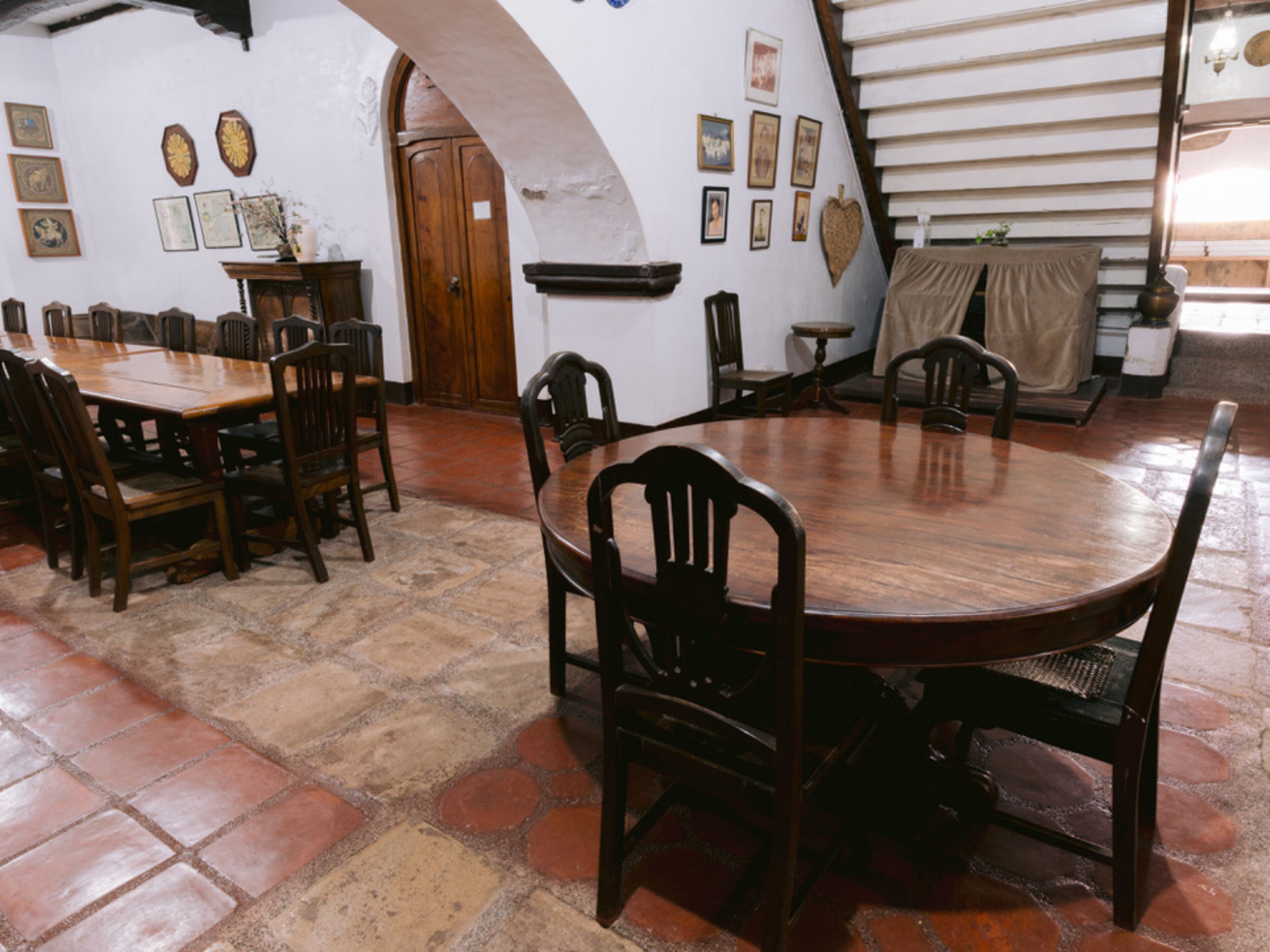 A dining area with a round wooden table and chairs, surrounded by a stone-tiled floor.
