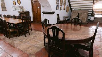 A dining area with a round wooden table and chairs, surrounded by a stone-tiled floor.