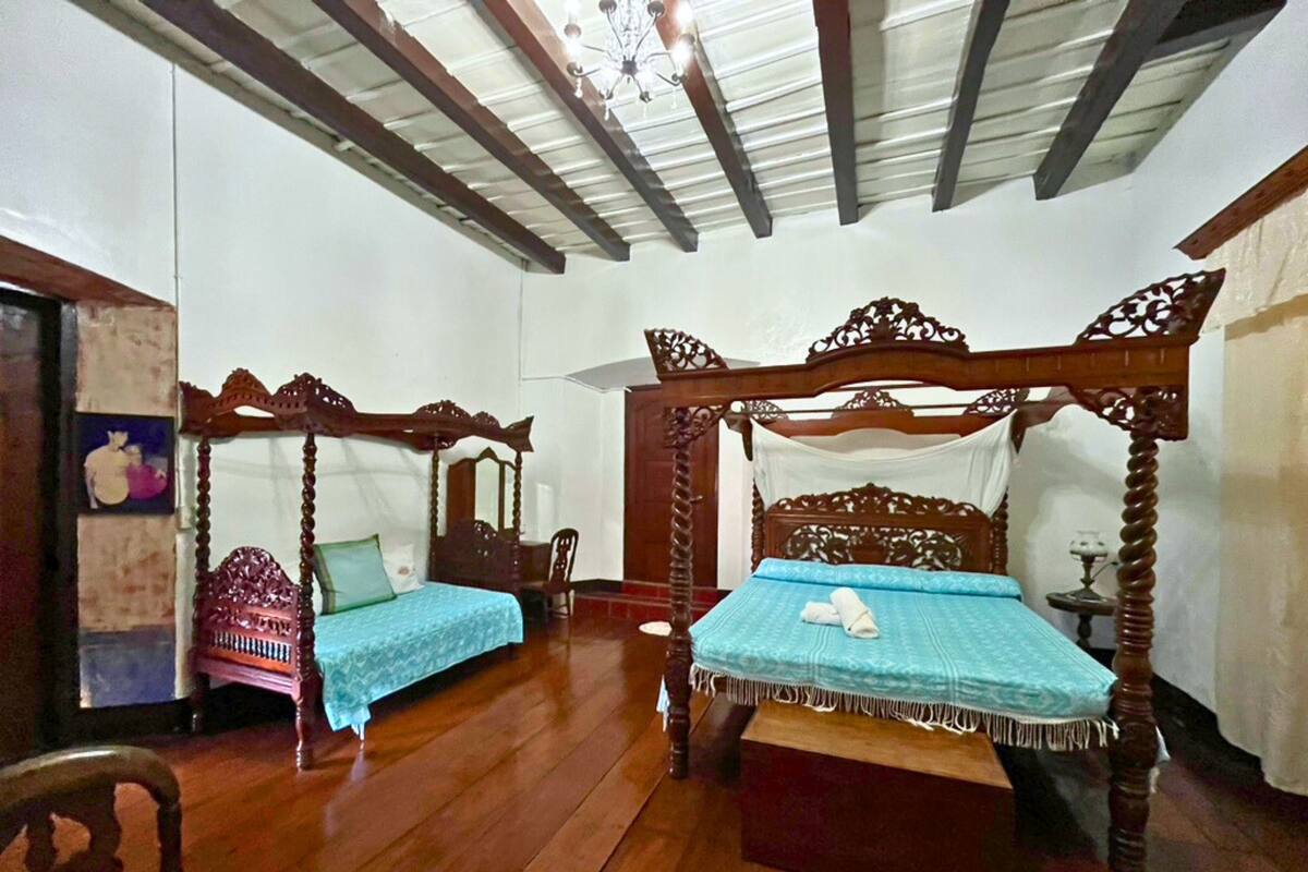 Una habitación con dos camas con dosel de madera, un candelabro y suelo de madera.