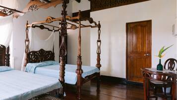 Un dormitorio tradicional con cama con dosel, una puerta de madera y una mesita con un florero.