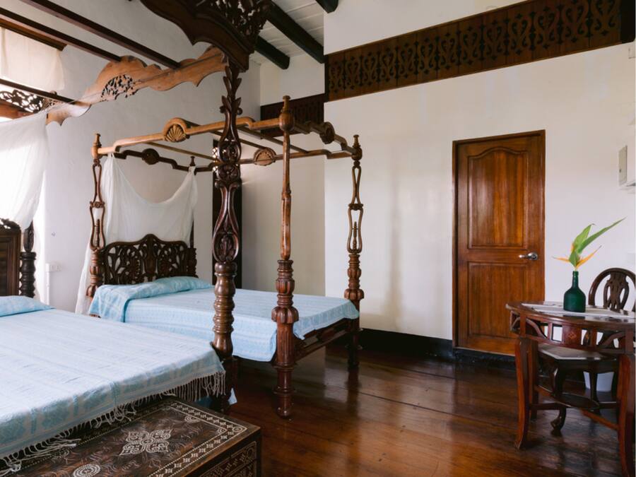 Un dormitorio tradicional con cama con dosel, una puerta de madera y una mesita con un florero.
