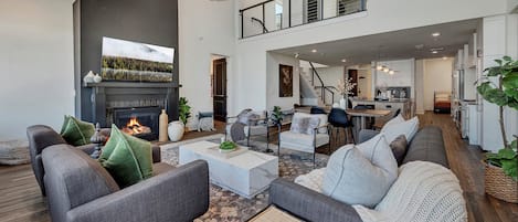 A spacious living area with a fireplace, sofas, a coffee table, and a kitchen in the background.