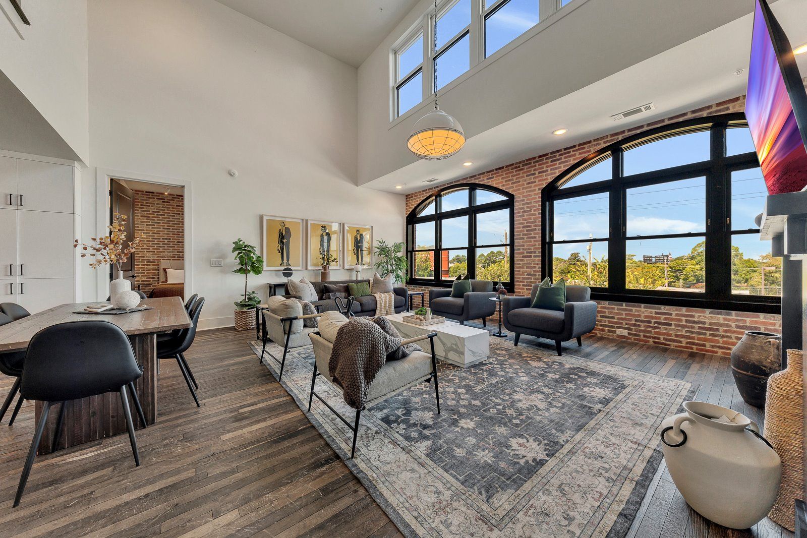 A spacious living area with a dining table, sofas, and large windows offering a view of the outdoors.