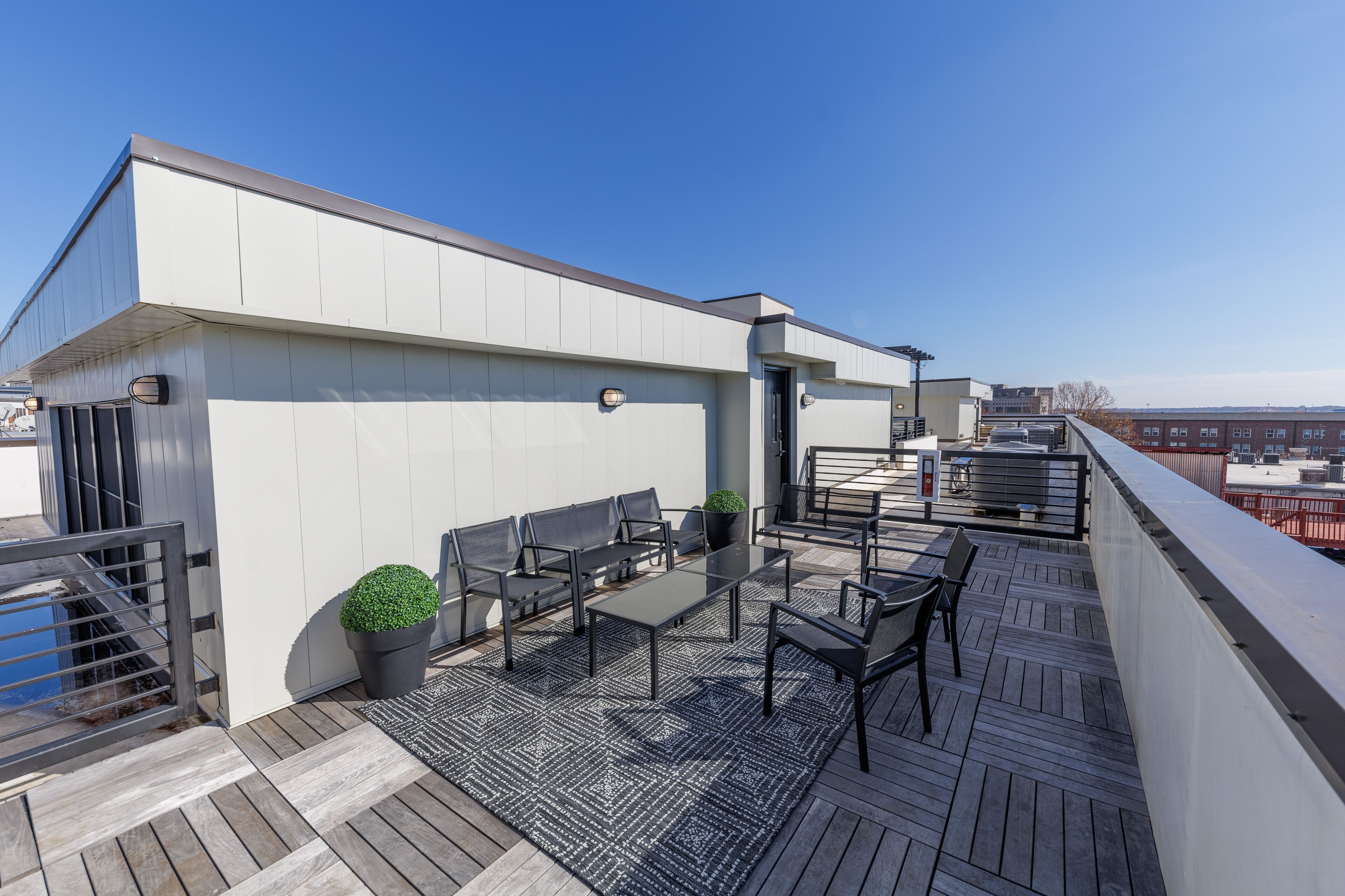 A rooftop terrace with a modern design, featuring a seating area with tables and chairs, a small potted plant, and a view of the cityscape.