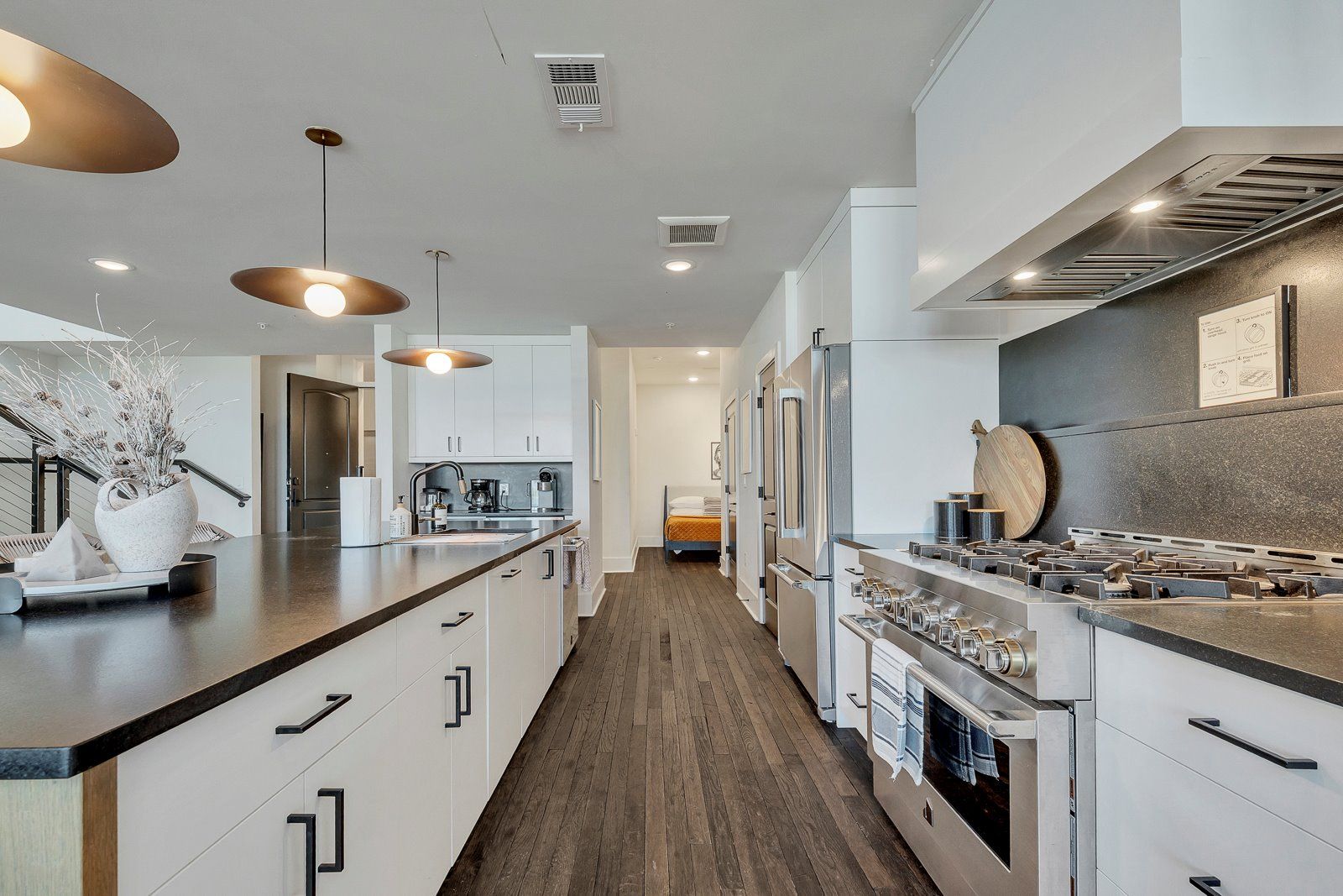 A modern kitchen with a central island, stainless steel appliances, pendant lighting, and a wooden floor.