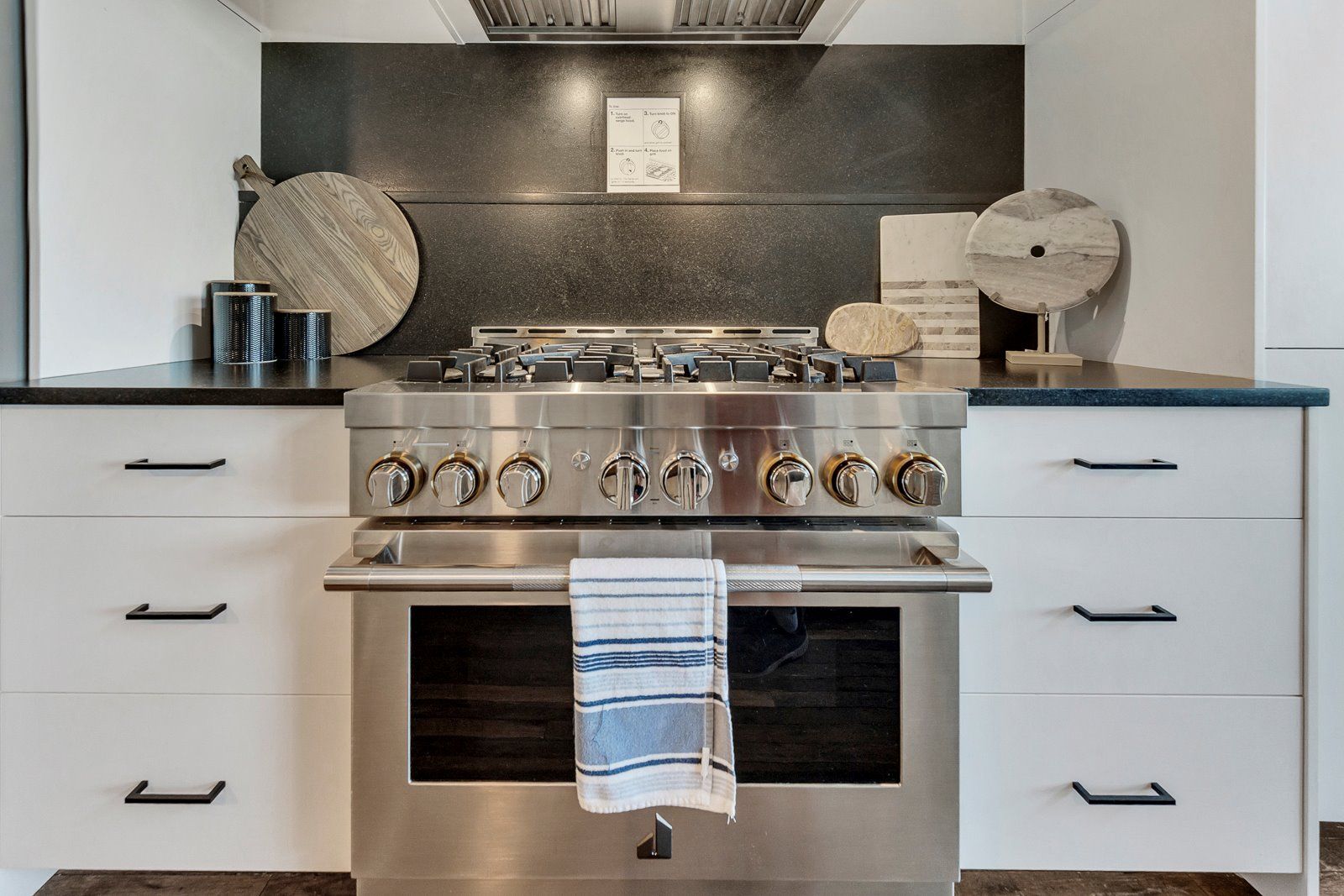 A modern kitchen with a stainless steel stove, white cabinetry, and a black backsplash.