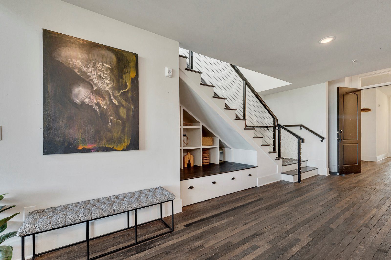 A modern interior with a staircase, a bench, and a large abstract painting.