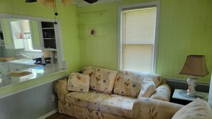 Una habitación con un sofá estampado con motivos florales, una mesita con una lámpara y una ventana con persianas.
