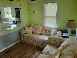 A room with a floral-patterned sofa, a small table with a lamp, and a window with blinds. - Spencerville Center House (Tallahassee)