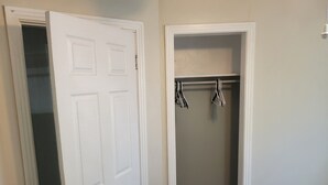 A room with a white door, a closet with hanging clothes, and a wooden floor. - Spencerville Center House (Tallahassee)