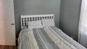 Un dormitorio con cama, puerta y ventana con cortinas.