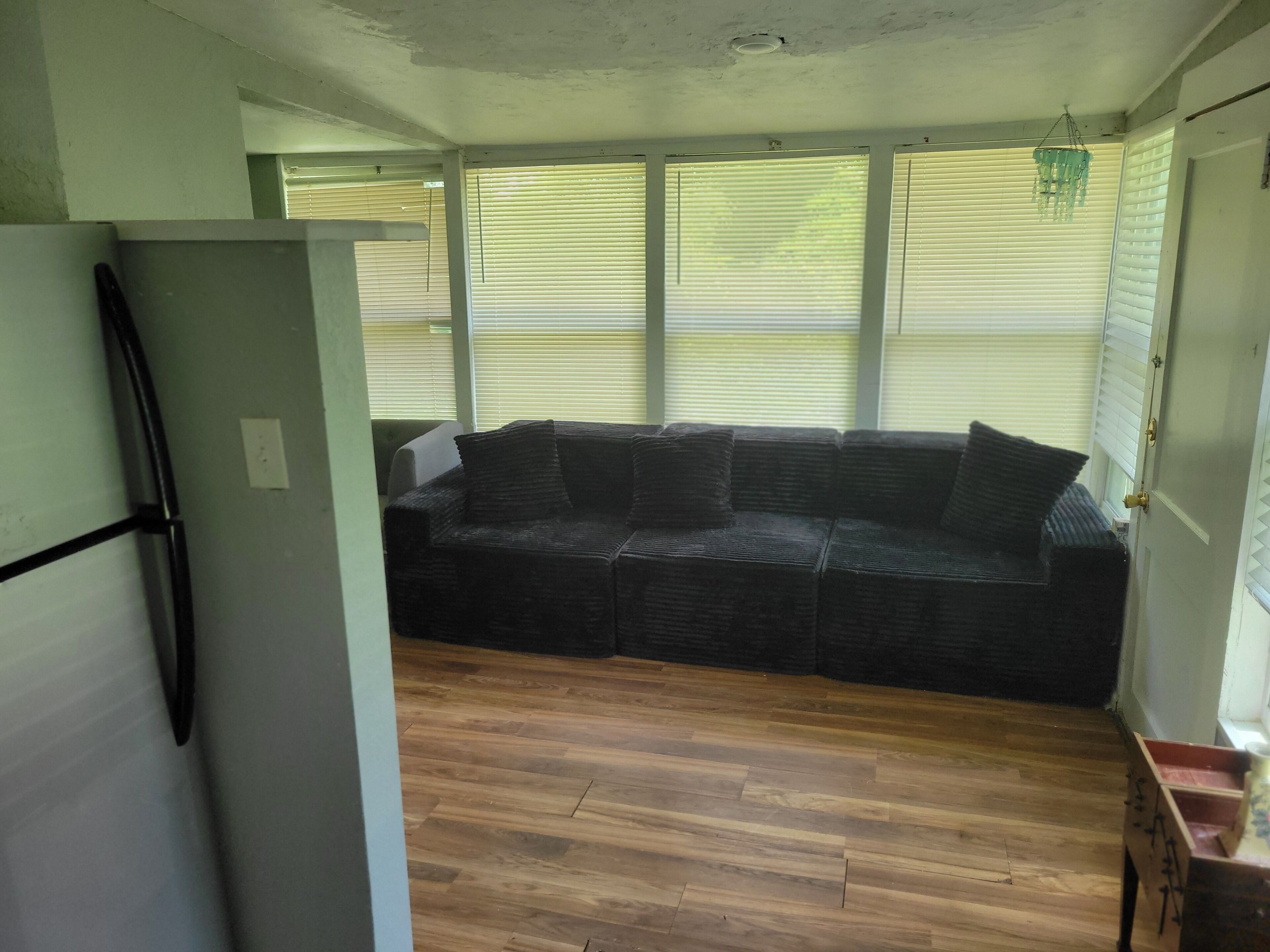 Ein Zimmer mit Holzboden, einer schwarzen Couch und einem weißen Kühlschrank.