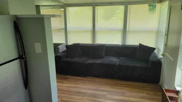 Een kamer met een houten vloer, een zwarte bank en een witte koelkast.