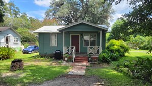 A green house with a front porch, a barbecue grill, and a car parked in the driveway. - Spencerville Center House (Tallahassee)