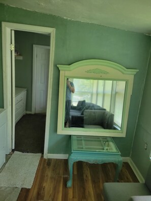 A room with a mirror on a glass-top table, a wooden floor, and a door leading to another room.