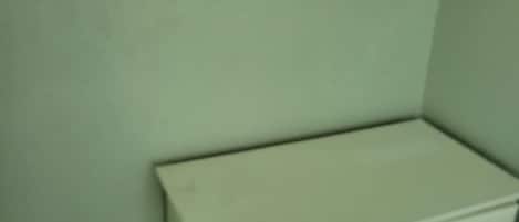 Un rincón de una habitación con un tocador blanco, un estante encima y una pared de color verde claro.