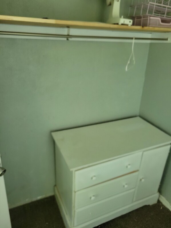 A corner of a room with a white dresser, a shelf above it, and a wall with a light green color.