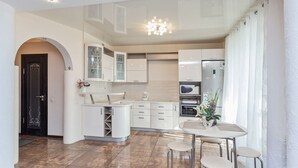Une cuisine moderne avec des meubles blancs, un four encastré et un coin repas comprenant une table et des tabourets.
