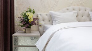 Un lit bien fait, avec du linge de lit blanc, une tête de lit capitonnée et une table de chevet dotée d'un tiroir orné d'un motif en mosaïque.