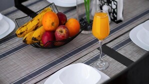 Ein Frühstückstisch mit Obstkorb, Orangensaft im Glas und ordentlich drapierten Tellern und Besteck auf einer gestreiften Tischdecke.
