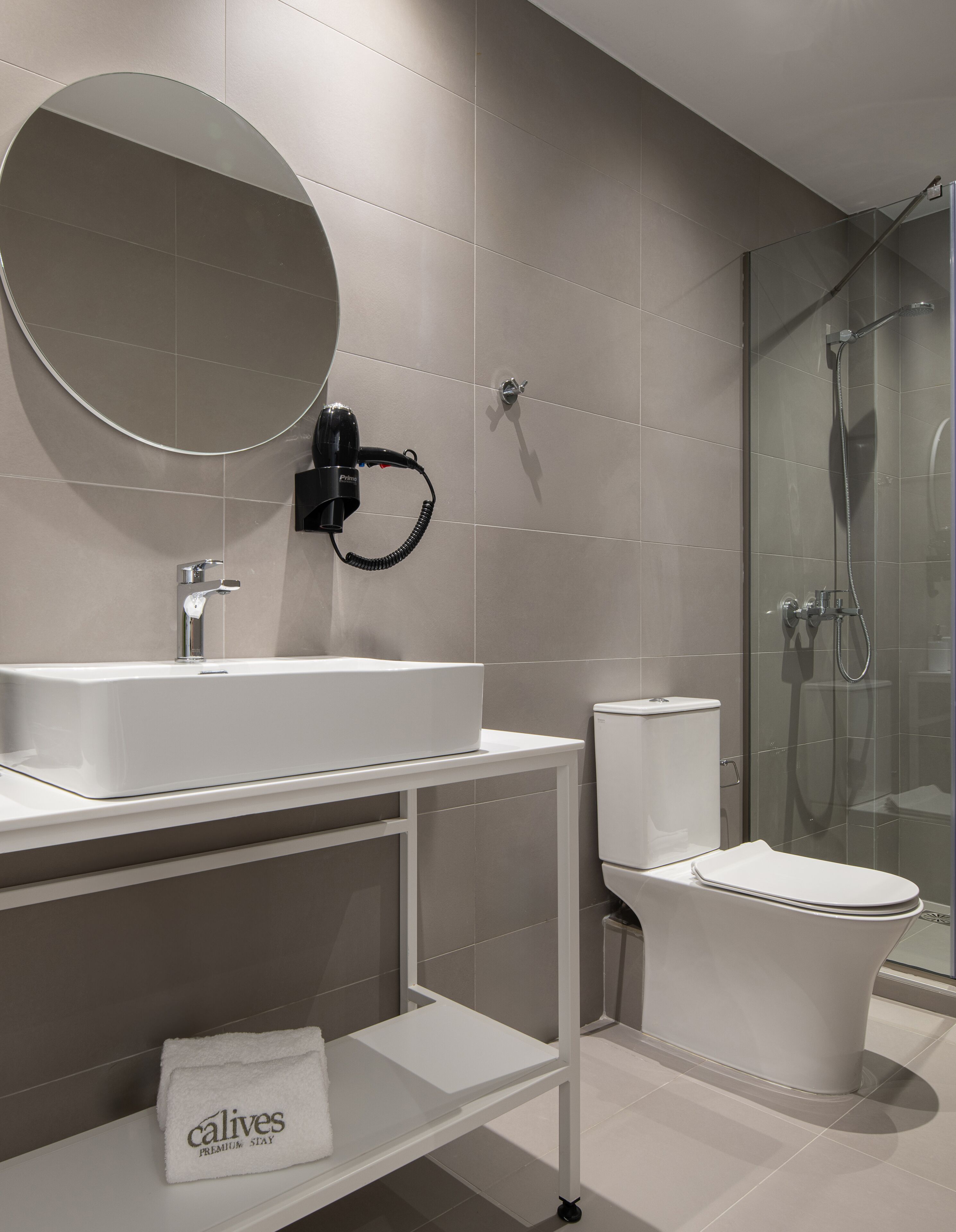 Un bagno moderno con uno specchio rotondo, un lavandino, un WC e una zona doccia.