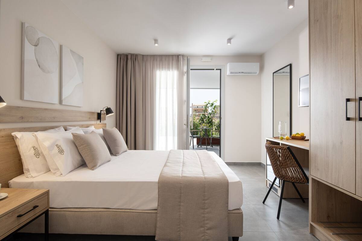 A modern hotel room with a large bed, a desk, and a view of the outdoors.