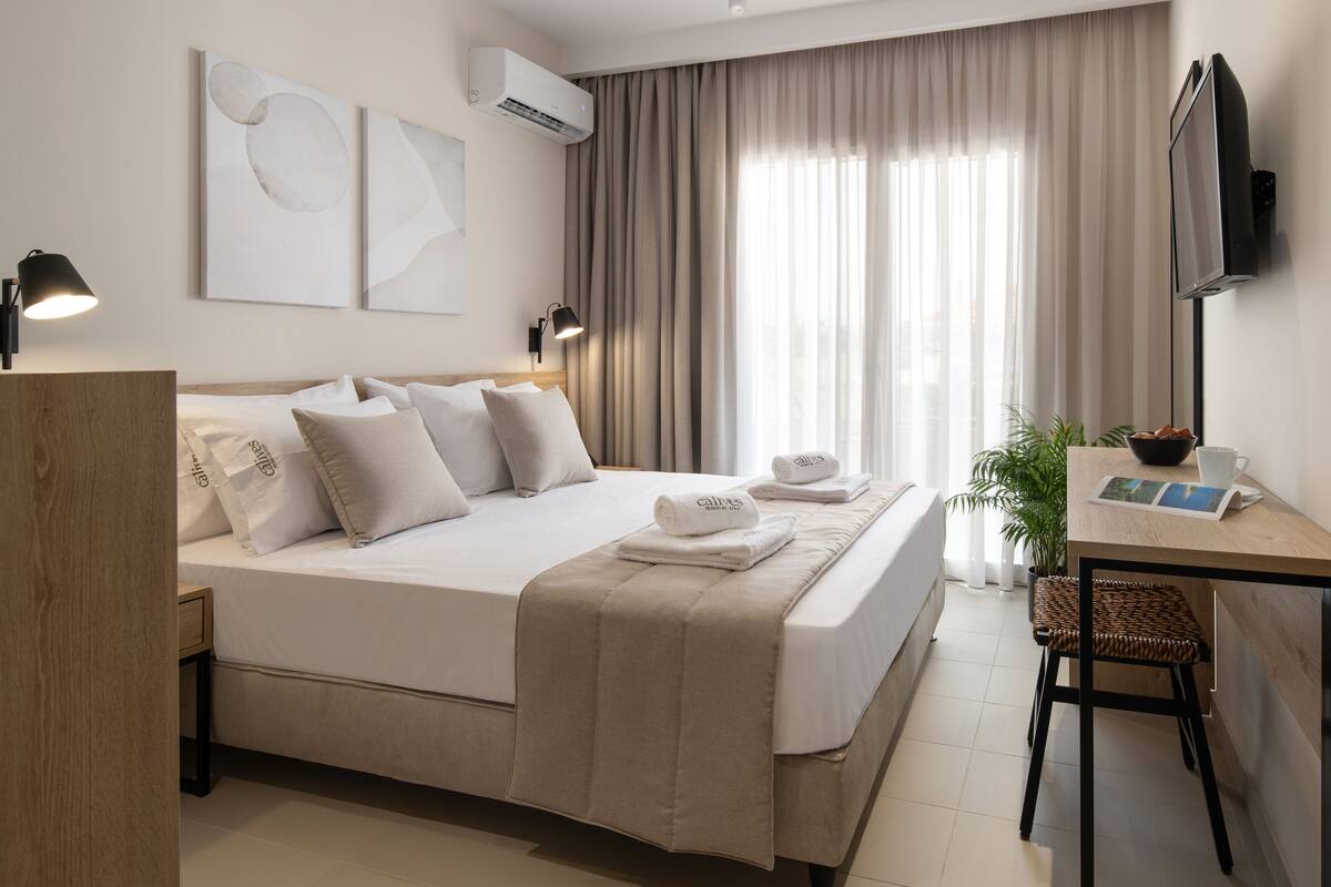 A hotel room with a bed, bedside lamps, a desk with a chair, a television, and a window with curtains.