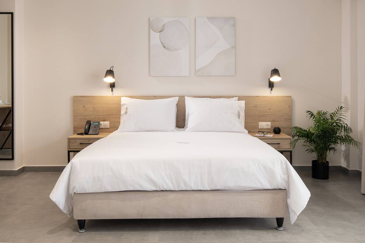 A modern hotel room with a large bed, bedside tables, a telephone, and a potted plant.