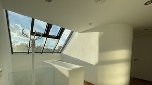 A modern, well-lit room with a skylight, a white sink, and a glass shower enclosure. - Luxurious Two Bedroom Penthouse (London)