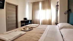 Ein Hotelzimmer mit Bett, Schreibtisch mit Stuhl, Fernseher an der Wand und einem Fenster mit Vorhängen.