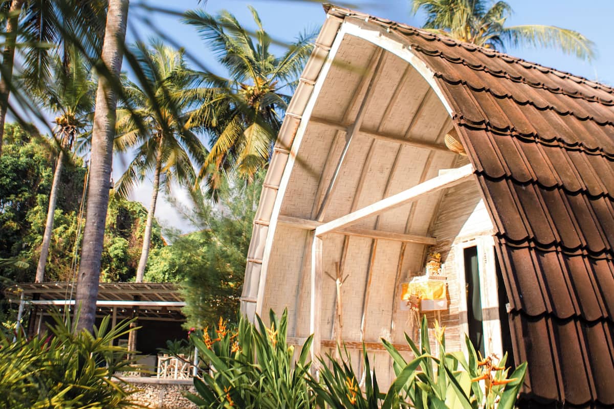 A small, rustic building with a curved roof, surrounded by lush greenery and palm trees.