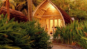 A rustic wooden cabin with a thatched roof, surrounded by lush greenery and a dirt path leading to the entrance. - La Royale Nusa Penida (Penida Island)