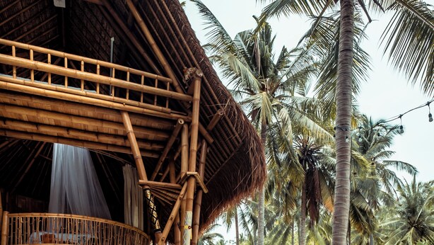 A woman sitting on a stone edge by a pool with a bamboo structure and palm trees in the background. - La Royale Nusa Penida (Penida Island)