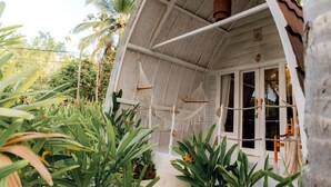 A white building with a sloped roof, a porch with hanging hammocks, and a view of palm trees. - La Royale Nusa Penida (Penida Island)