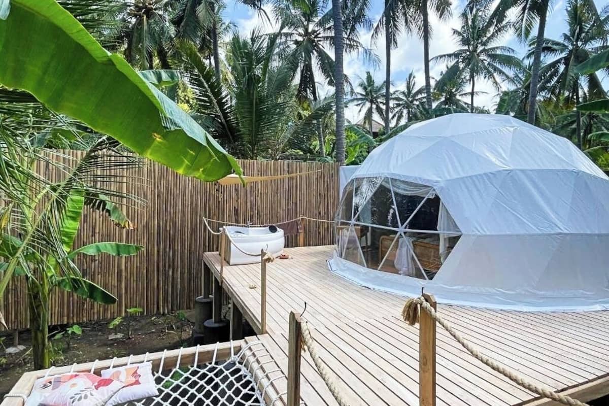 A white dome tent on a wooden deck with a bamboo fence and a hammock.