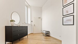 Ein modernes, minimalistisches Zimmer mit Holzboden, einem schwarzen Konsolentisch mit Spiegel und Topfpflanze sowie einer Tür zu einem anderen Raum.
