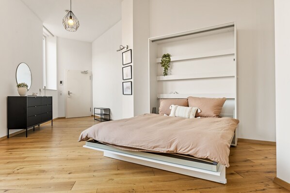 A modern bedroom with a bed, a dresser, a mirror, and a wall-mounted shelf with a plant.