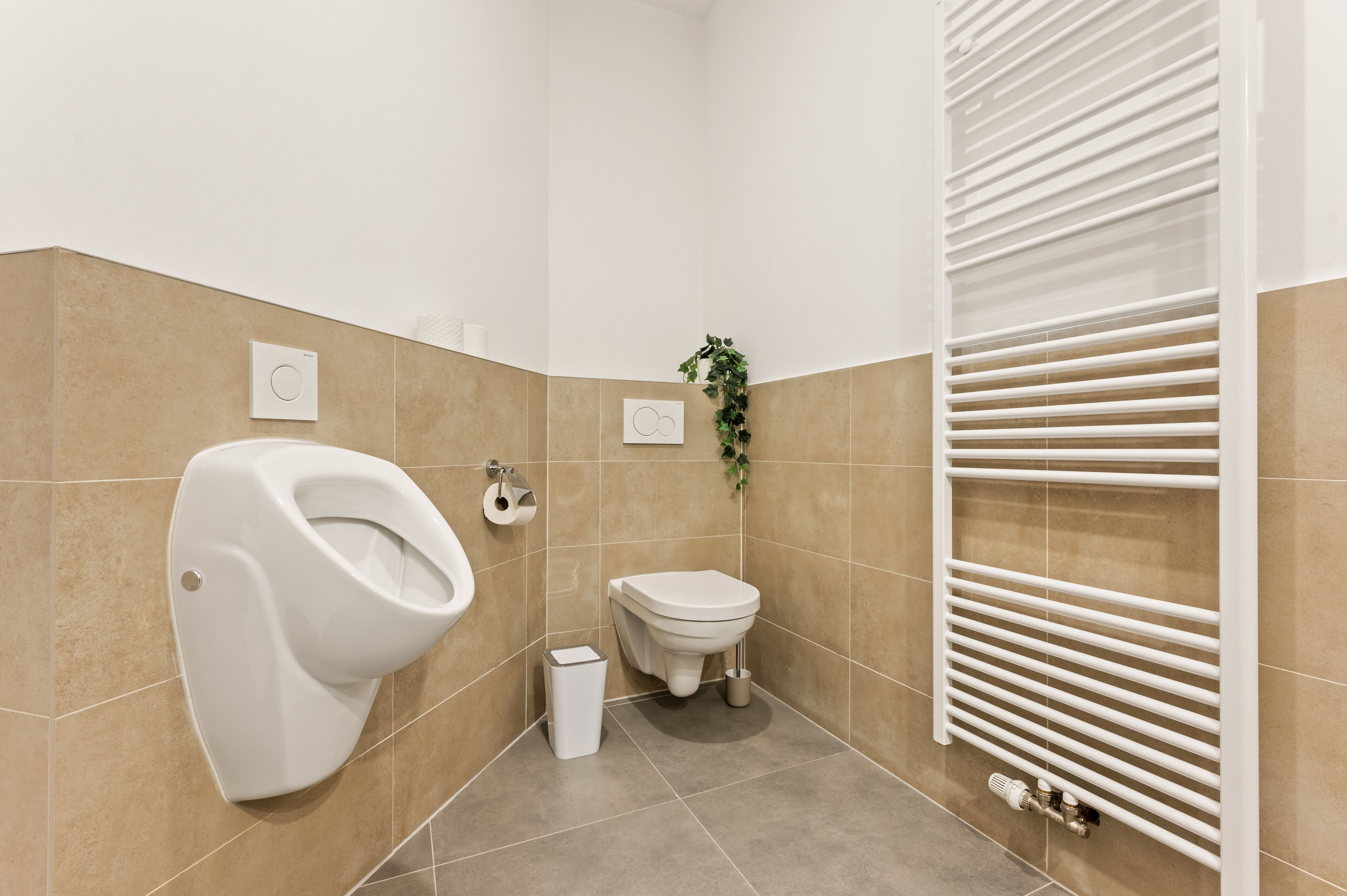 Un baño moderno con orinal, inodoro y radiador.