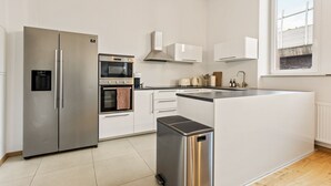 Eine moderne Küche mit einem Edelstahl-Kühlschrank, Backofen und einer Mikrowelle. Ein kleiner Mülleimer und ein Fenster sorgen für natürliches Licht.