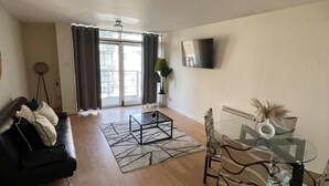 Un salon moderne avec une table basse en verre, un canapé noir et un coin repas comprenant une table et des chaises en verre.