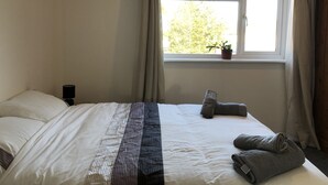 A neatly made bed with a striped blanket, a potted plant on the windowsill, and a bedside lamp. - Comfy modern townhouse/w free parking & garden, newly refurbished, self catering (Cheltenham)