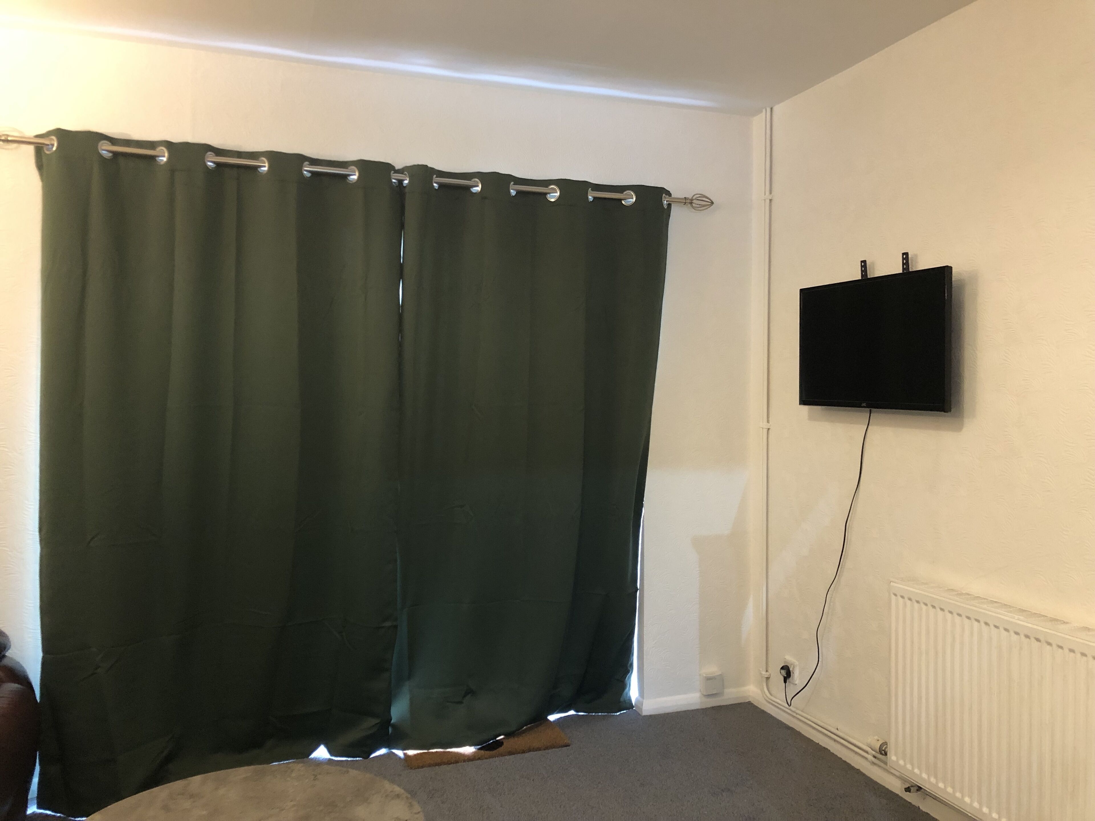 A room with a green curtain, a mounted TV, and a radiator.