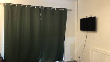 A room with a green curtain, a mounted TV, and a radiator.