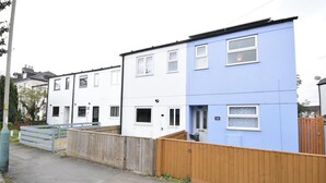 A row of terraced houses with a wooden fence in the foreground. - Comfy modern townhouse/w free parking & garden, newly refurbished, self catering (Cheltenham)